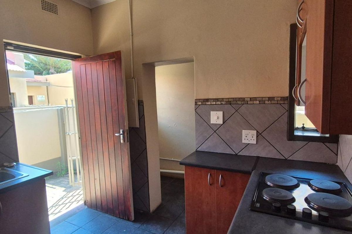 A functional kitchen featuring dark cabinetry, a built-in electric hob, tiled backsplash, and direct access to an outdoor area.