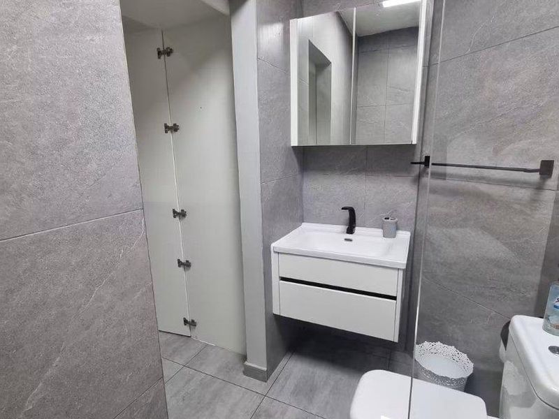 Modern bathroom featuring grey floor-to-ceiling tiles, a wall-mounted vanity with basin, mirrored medicine cabinet, and a glass shower screen.