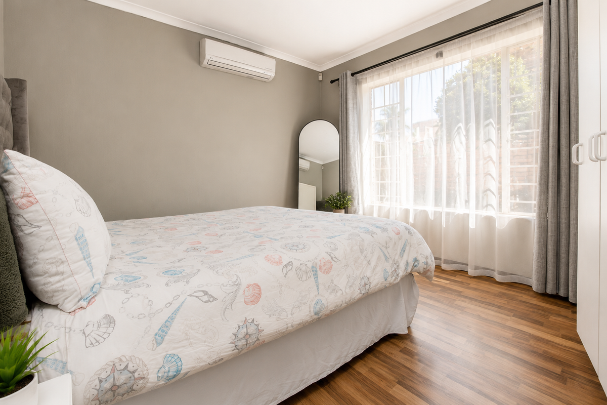 A well-maintained bedroom featuring laminate flooring, a wall-mounted air conditioning unit, and a built-in wardrobe with natural light from the large window.