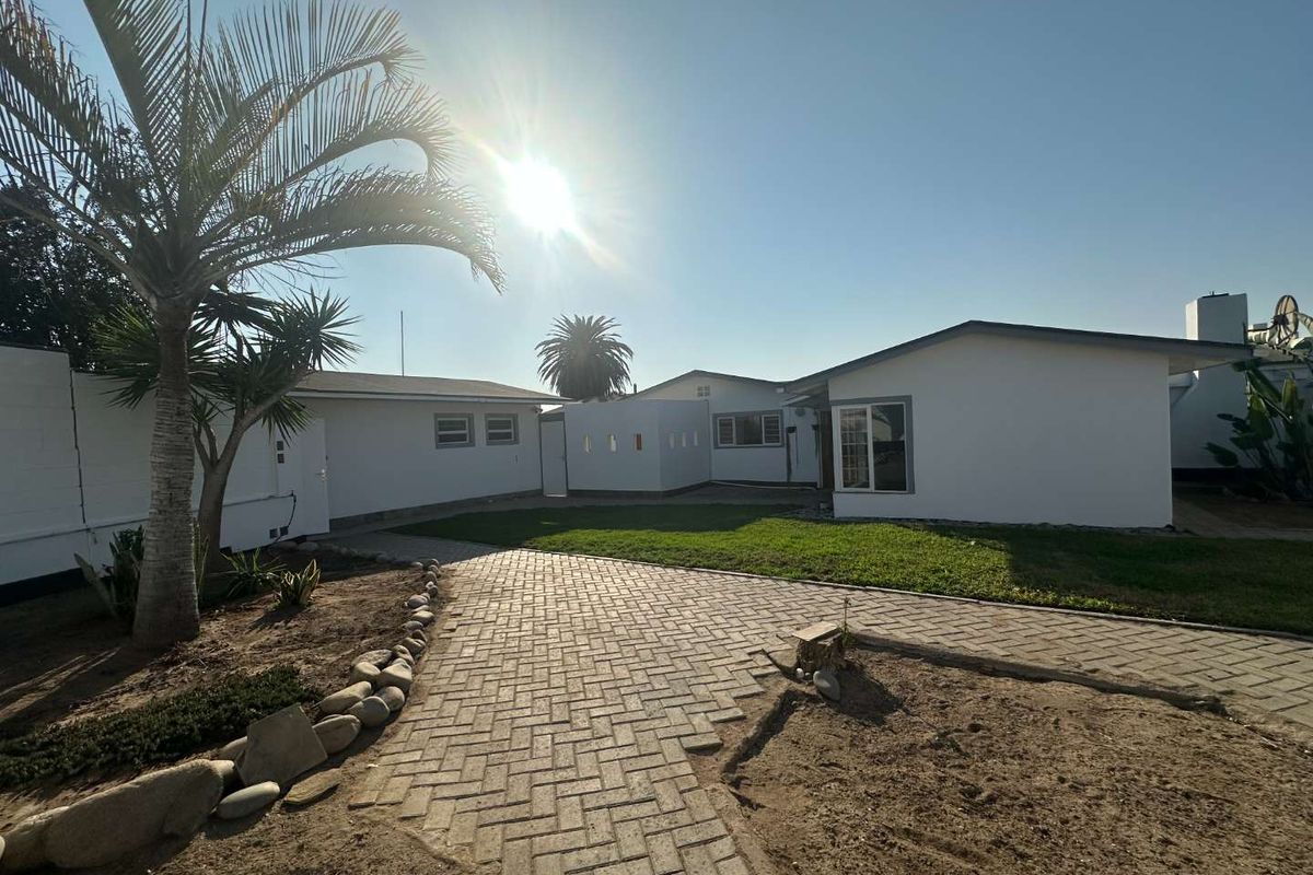 Rear exterior view of the property featuring a paved walkway, lawn area, and white painted building facade.