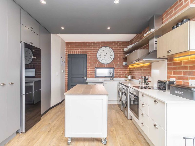 Modern kitchen featuring exposed brick walls, sleek cabinetry, integrated appliances, and recessed lighting, offering a stylish and functional culinary space.