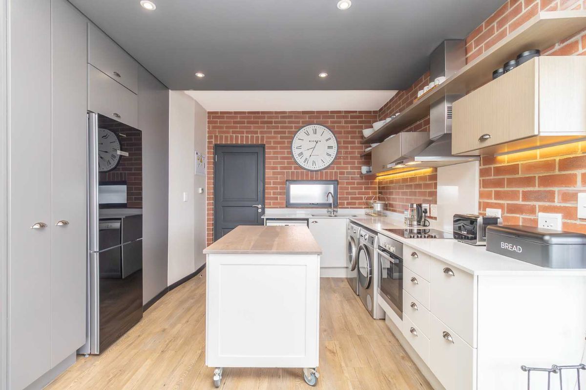 Modern kitchen featuring exposed brick walls, sleek cabinetry, integrated appliances, and recessed lighting, offering a stylish and functional culinary space.