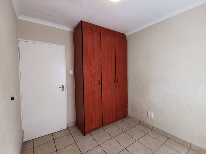 A clean, empty bedroom featuring neutral wall finishes, tiled flooring, and a built-in wooden wardrobe.
