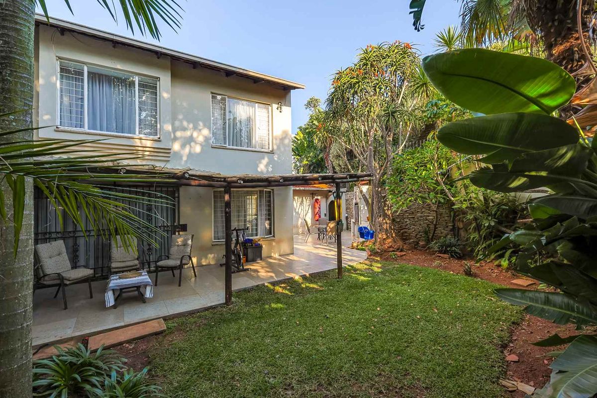 Rear view of the townhouse featuring a paved patio area with a timber pergola, overlooking a private garden with established trees and landscaping.