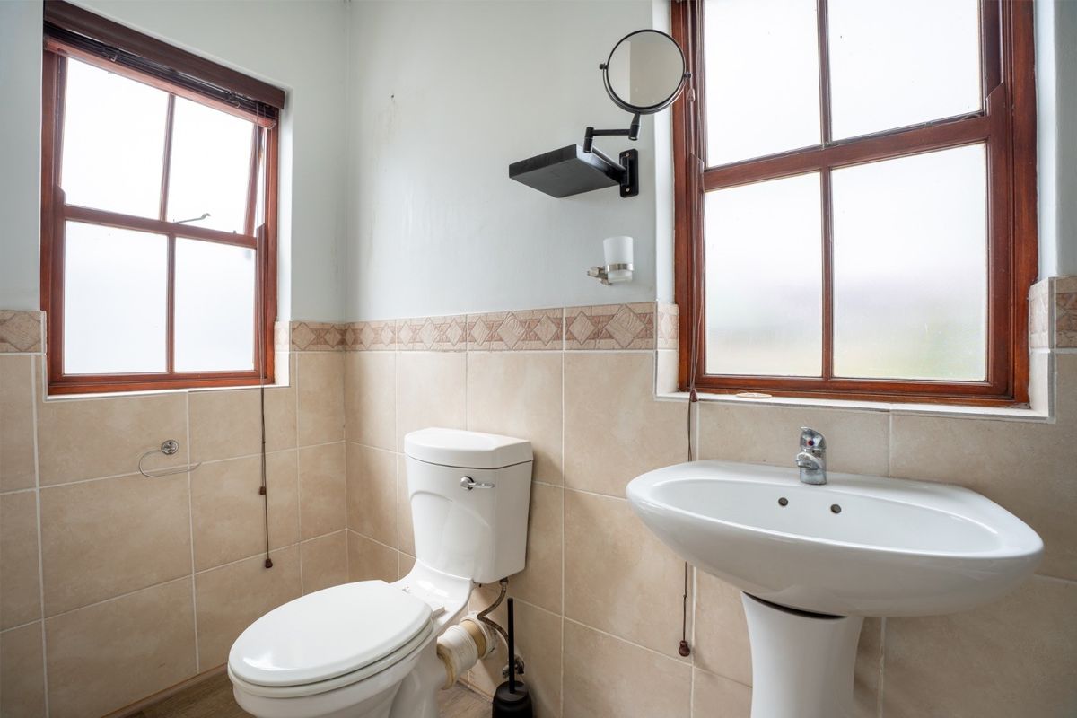 A functional bathroom featuring a pedestal basin, toilet, and tiled walls with timber-framed windows providing natural light.