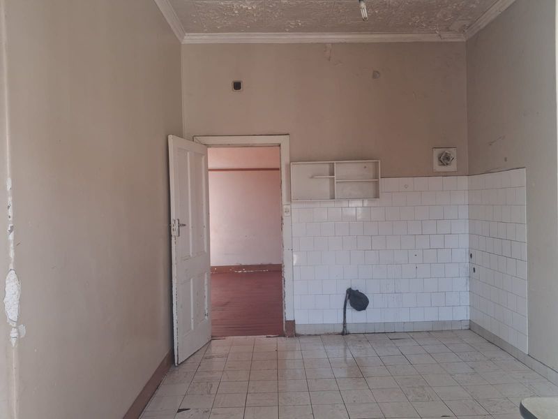 An empty, dated kitchen space featuring tiled flooring and splashbacks, requiring significant renovation and cosmetic updates to restore its functionality and appeal.