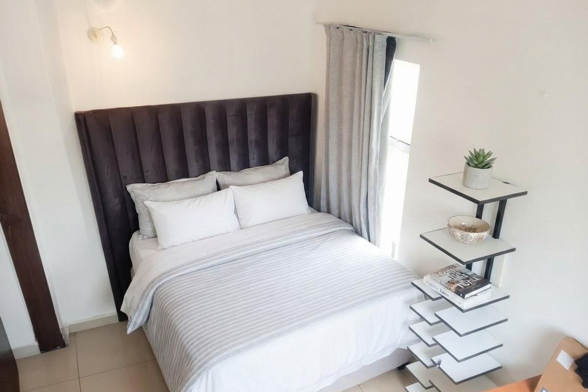 A well-lit bedroom featuring neutral tiled flooring, a modern wall-mounted light fixture, and a window dressed with curtains.