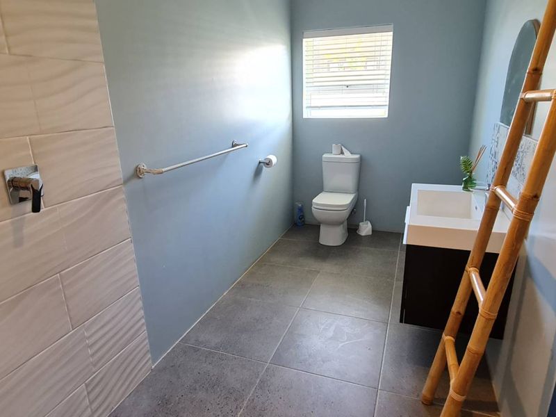 A modern bathroom featuring a wall-mounted vanity, tiled shower area, and neutral floor tiles, offering a clean and functional layout.