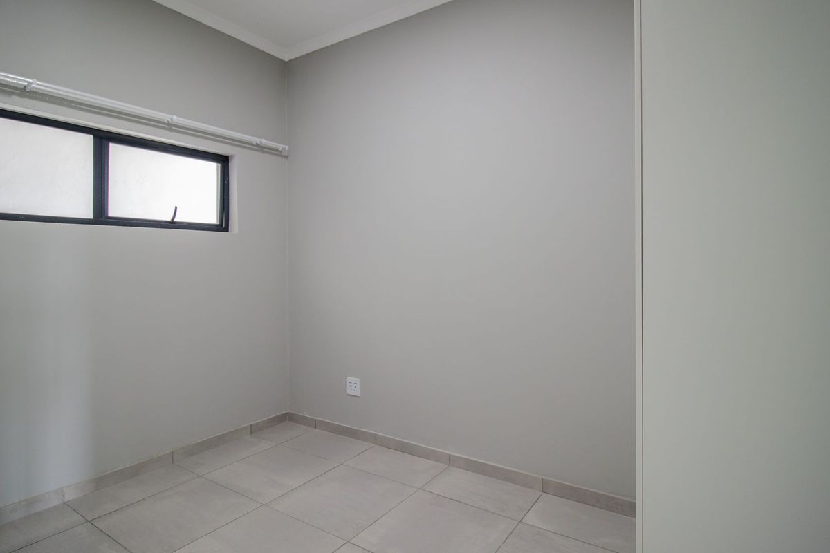 A clean, empty bedroom featuring neutral tiled flooring, a built-in cupboard, and an aluminium-framed window, offering a blank canvas for personalization.