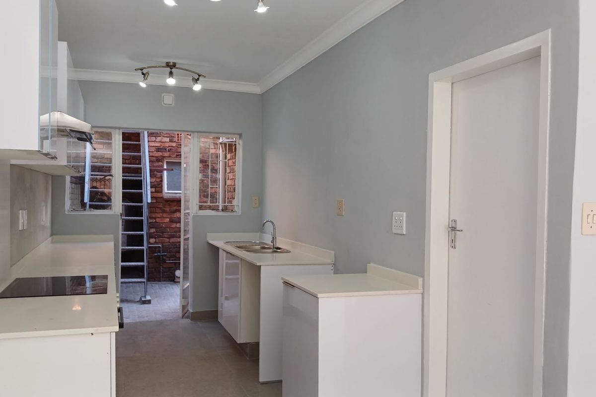 A clean, modern kitchen featuring white cabinetry, integrated hob, extractor fan, and direct access to a rear courtyard area.