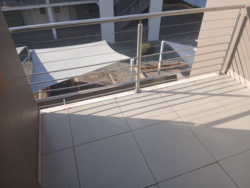 A clean, tiled balcony featuring a modern stainless steel and cable balustrade, overlooking the apartment complex parking area.