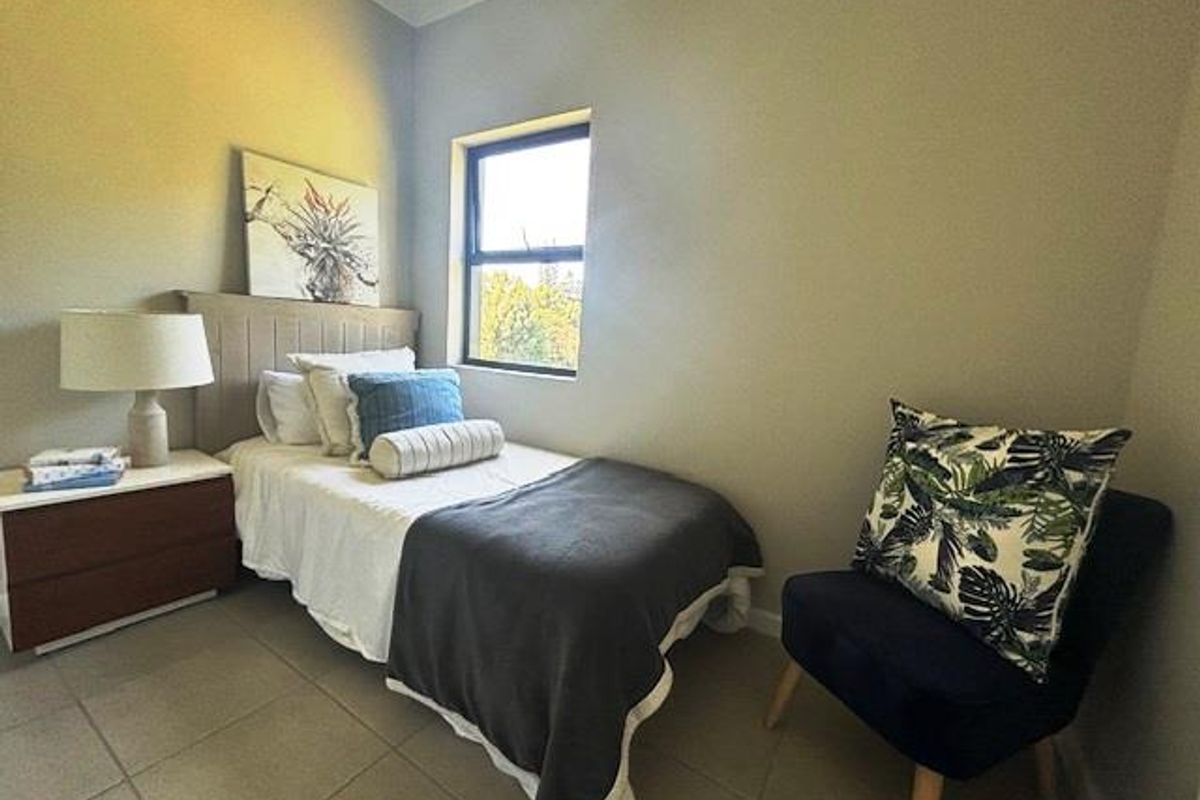 A compact bedroom featuring neutral tiled flooring, a single window providing natural light, and a neutral wall finish.