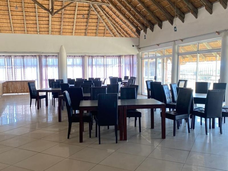 Spacious dining area featuring a high vaulted thatched roof with exposed timber trusses, large glass sliding doors, and neutral tiled flooring.