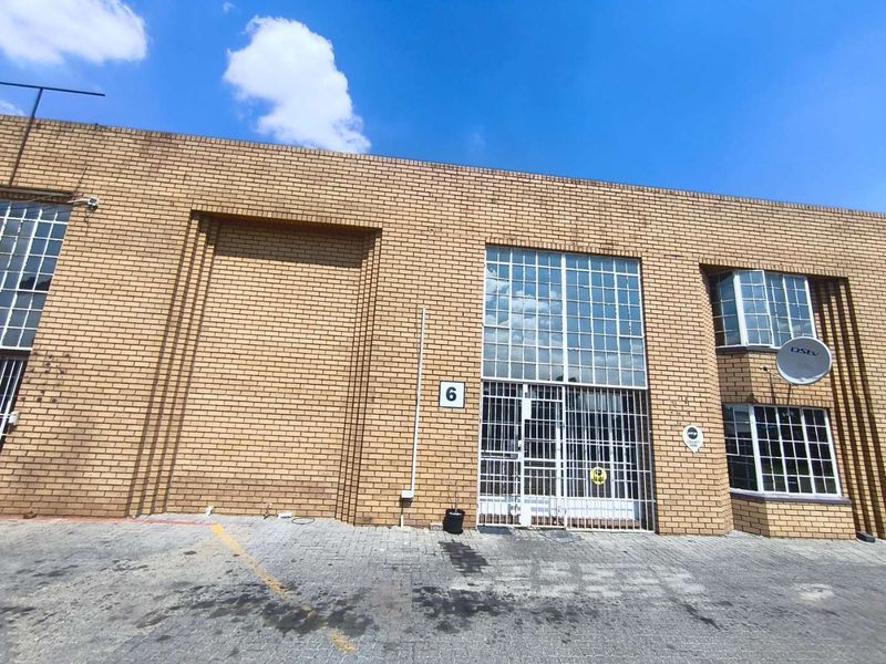 Front elevation of an industrial unit featuring face brick construction, steel-framed windows with security bars, and a paved driveway area.