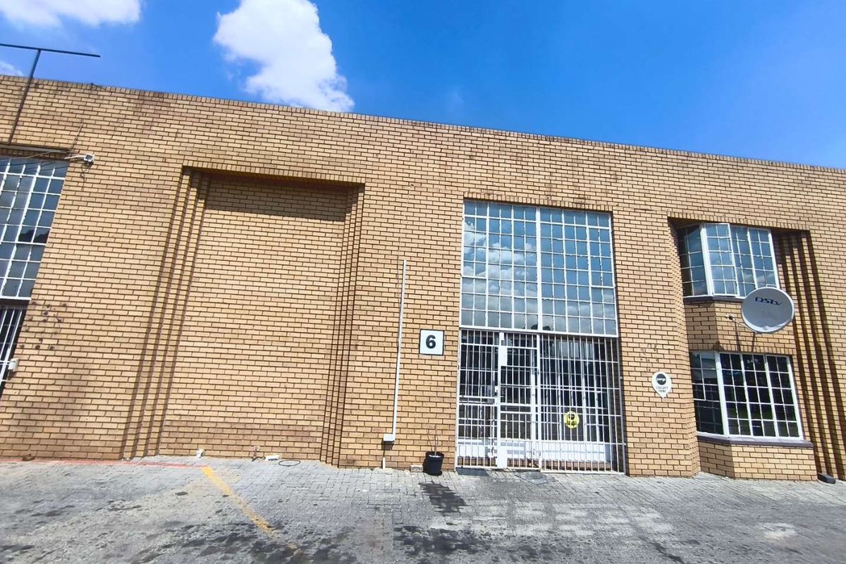 Front elevation of an industrial unit featuring face brick construction, steel-framed windows with security bars, and a paved driveway area.