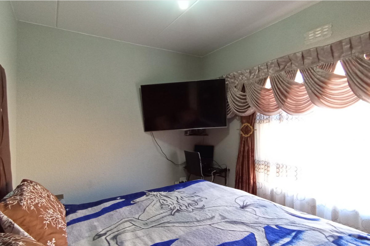 A bedroom featuring a wall-mounted television and a large window with decorative valance curtains.
