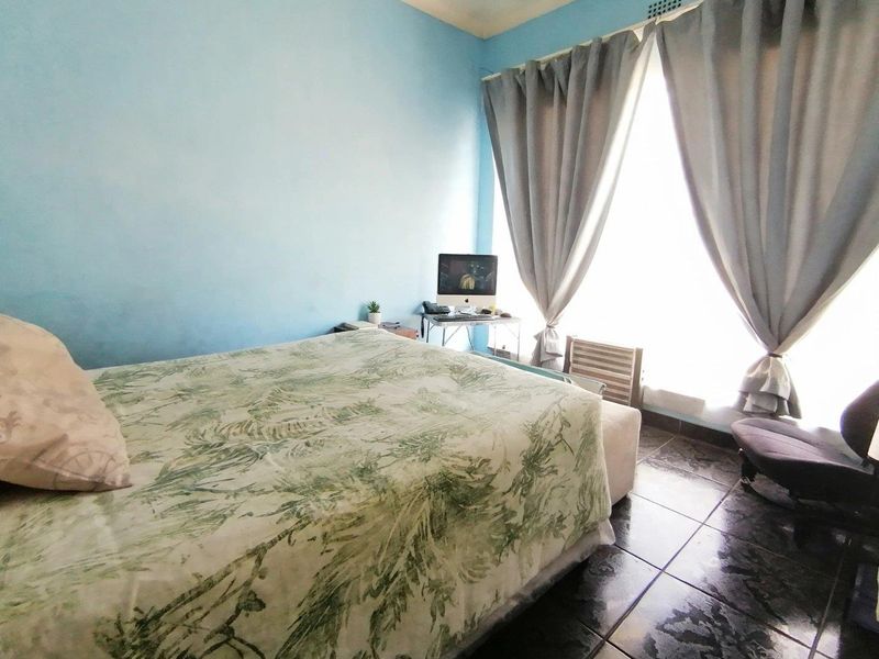 A bedroom featuring dark tiled flooring and a large window with curtains, providing natural light to the space.