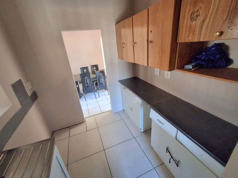 A functional scullery or utility area featuring built-in wooden cabinetry, laminate countertops, and tiled flooring, providing additional prep and storage space.