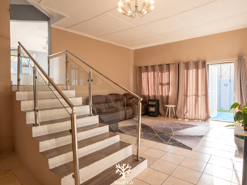 Spacious living area featuring a modern staircase with glass balustrades, tiled flooring, and direct access to the outdoor area through a sliding door.