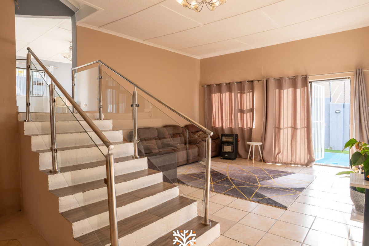 Spacious living area featuring a modern staircase with glass balustrades, tiled flooring, and direct access to the outdoor area through a sliding door.