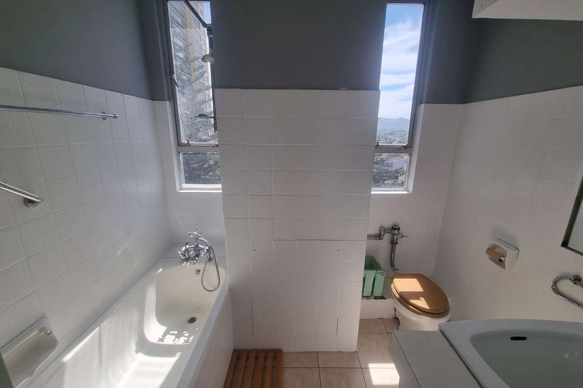 A functional bathroom featuring a bathtub, toilet, and washbasin with tiled finishes and natural light from two windows.