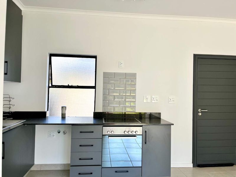 Modern kitchen featuring grey cabinetry, granite countertops, a built-in oven with electric hob, and a stylish subway tile backsplash.
