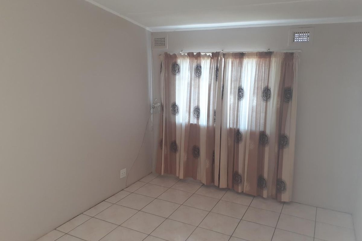 A simple, empty bedroom featuring neutral wall paint, tiled flooring, and built-in ventilation vents.