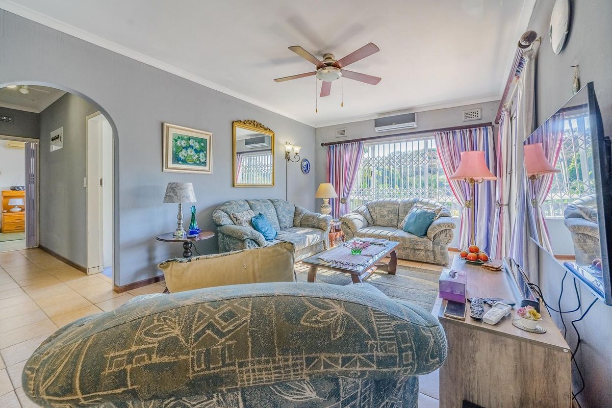 A comfortable living room featuring tiled flooring, a ceiling fan, and a wall-mounted air conditioning unit, with an arched entryway leading to other areas.