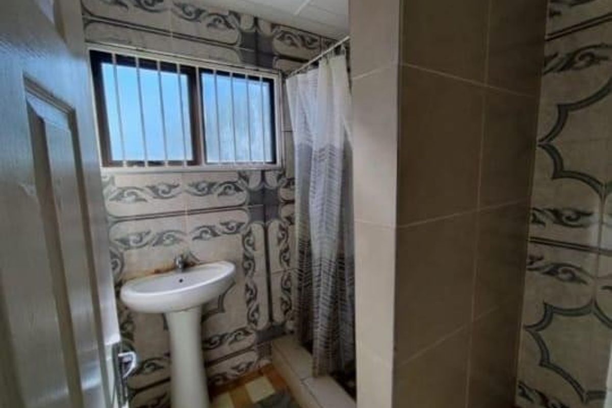 A compact bathroom featuring a pedestal basin, shower area with curtain, and patterned wall tiling. The space requires cosmetic updates to improve its condition.