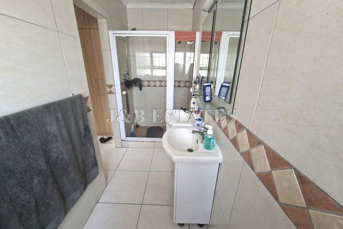 A functional bathroom featuring a pedestal sink, a glass-enclosed shower, and neutral wall tiling with a decorative accent border.