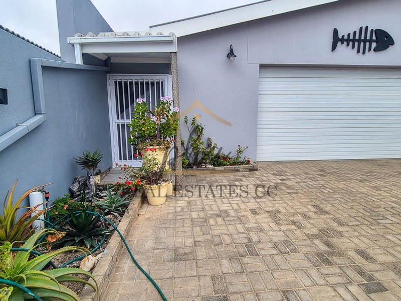 Front exterior view of the property featuring a paved driveway, automated garage door, and a secure entrance gate.