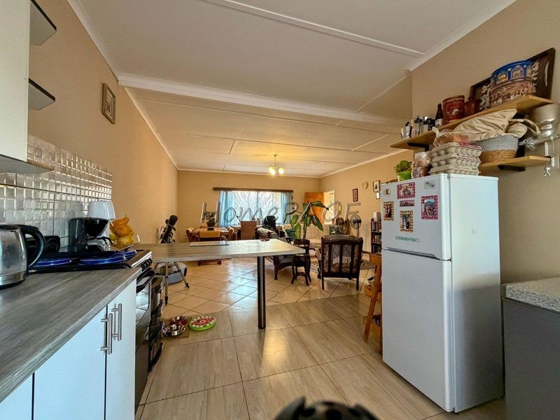 Open-plan living area featuring a functional kitchen with breakfast bar, tiled flooring, and neutral wall tones, flowing into the dining and lounge space.