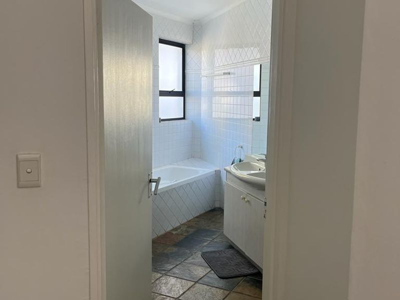 A functional bathroom featuring a built-in vanity with basin, a tiled bathtub, and slate flooring, offering potential for modern updates.