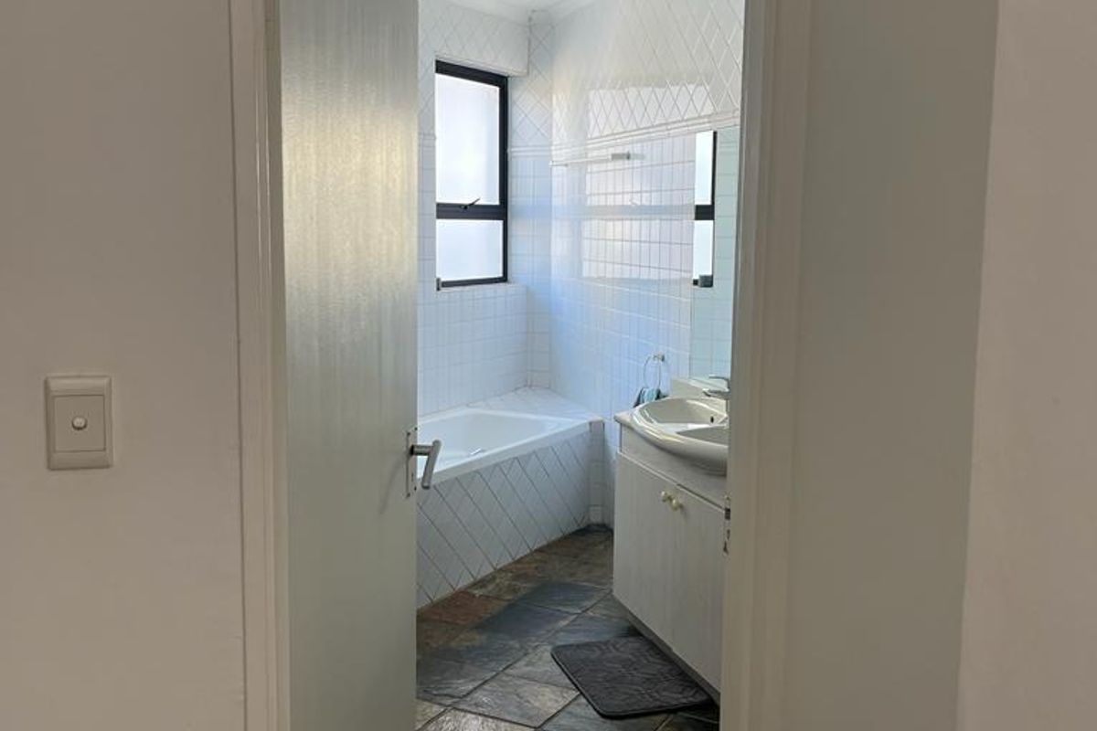 A functional bathroom featuring a built-in vanity with basin, a tiled bathtub, and slate flooring, offering potential for modern updates.