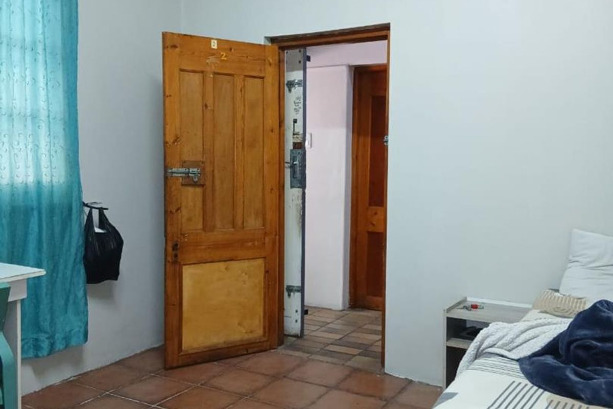 A functional bedroom featuring tiled flooring, a wooden door, and access to an adjoining hallway.