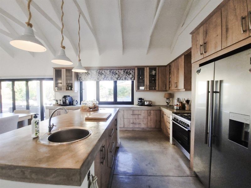 Modern kitchen featuring concrete countertops, a central island with sink, built-in cabinetry, gas stove, and vaulted ceilings with exposed beams.