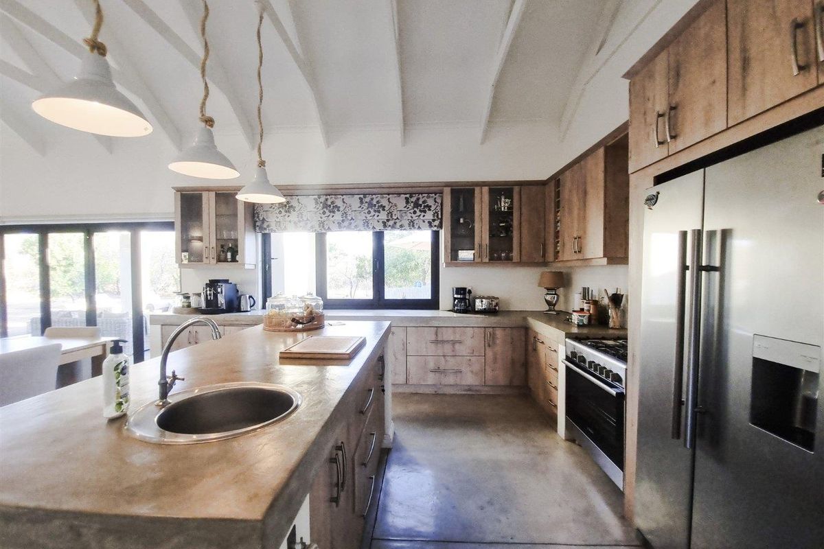 Modern kitchen featuring concrete countertops, a central island with sink, built-in cabinetry, gas stove, and vaulted ceilings with exposed beams.