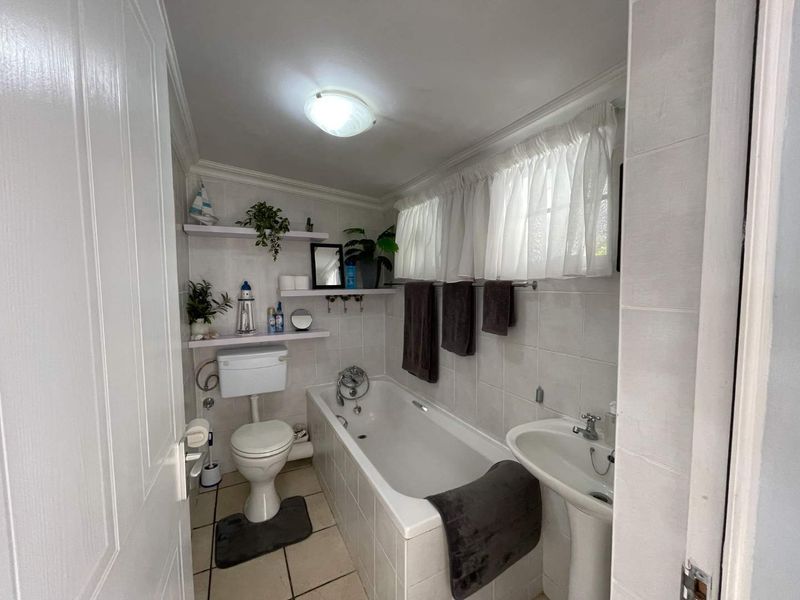 A functional bathroom featuring a bathtub, pedestal basin, toilet, and neutral tiled finishes, offering a clean and practical space.