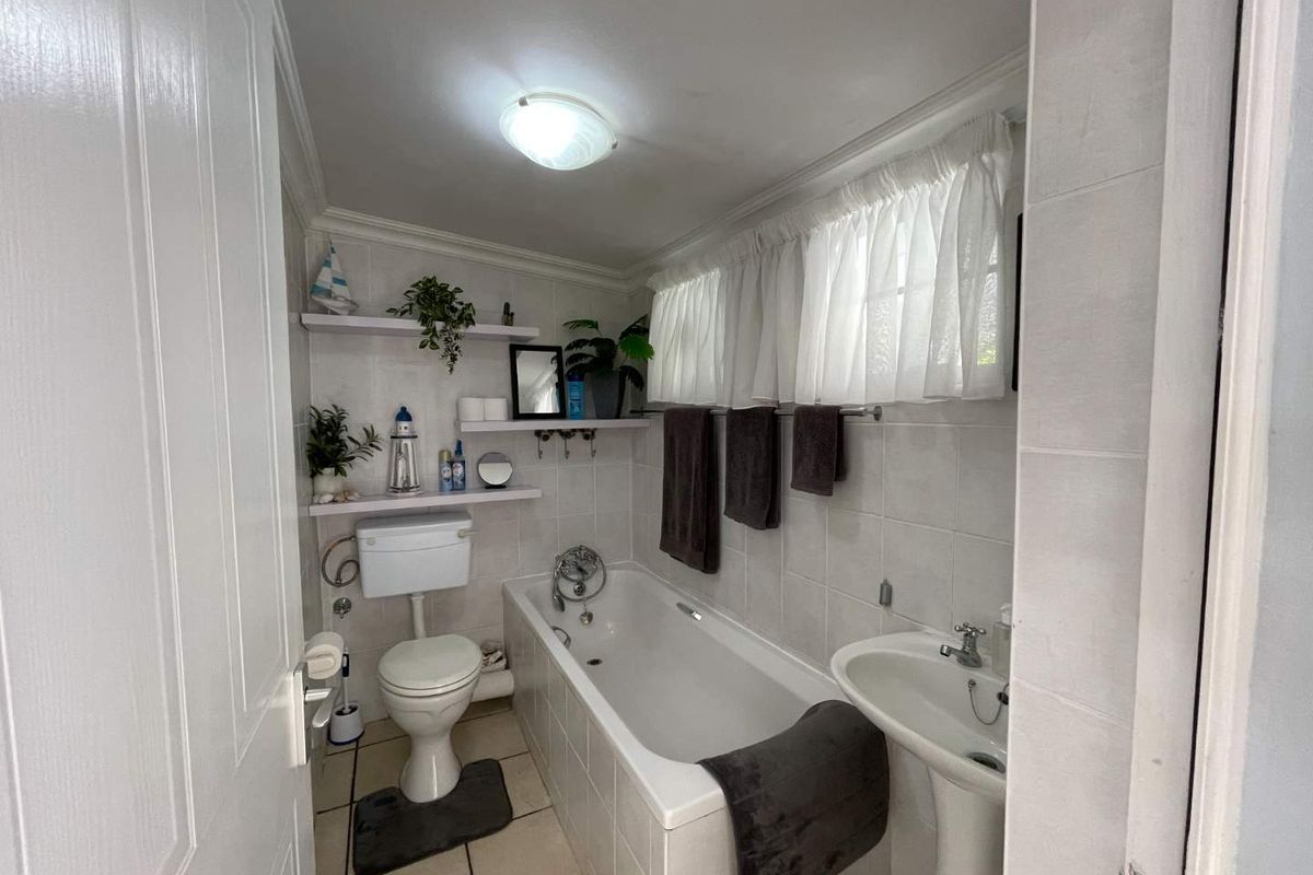 A functional bathroom featuring a bathtub, pedestal basin, toilet, and neutral tiled finishes, offering a clean and practical space.