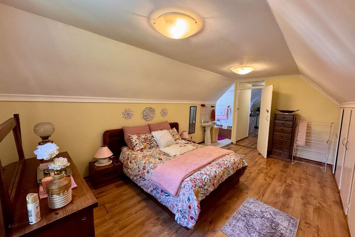 Spacious attic-style bedroom featuring sloped ceilings, laminate wood flooring, and an en-suite bathroom area with a pedestal basin.