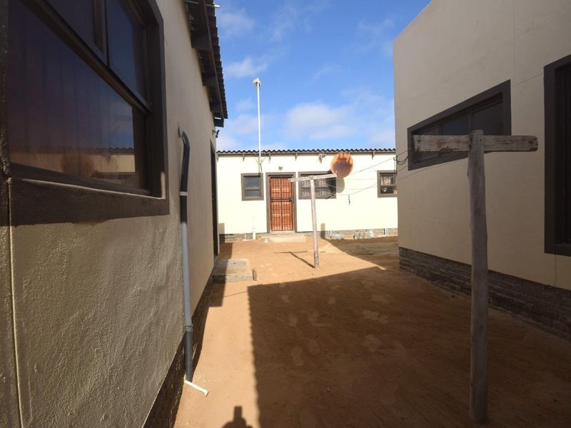 Rear exterior courtyard area featuring unpaved ground, security gate access, and exterior building walls with dark window frames.