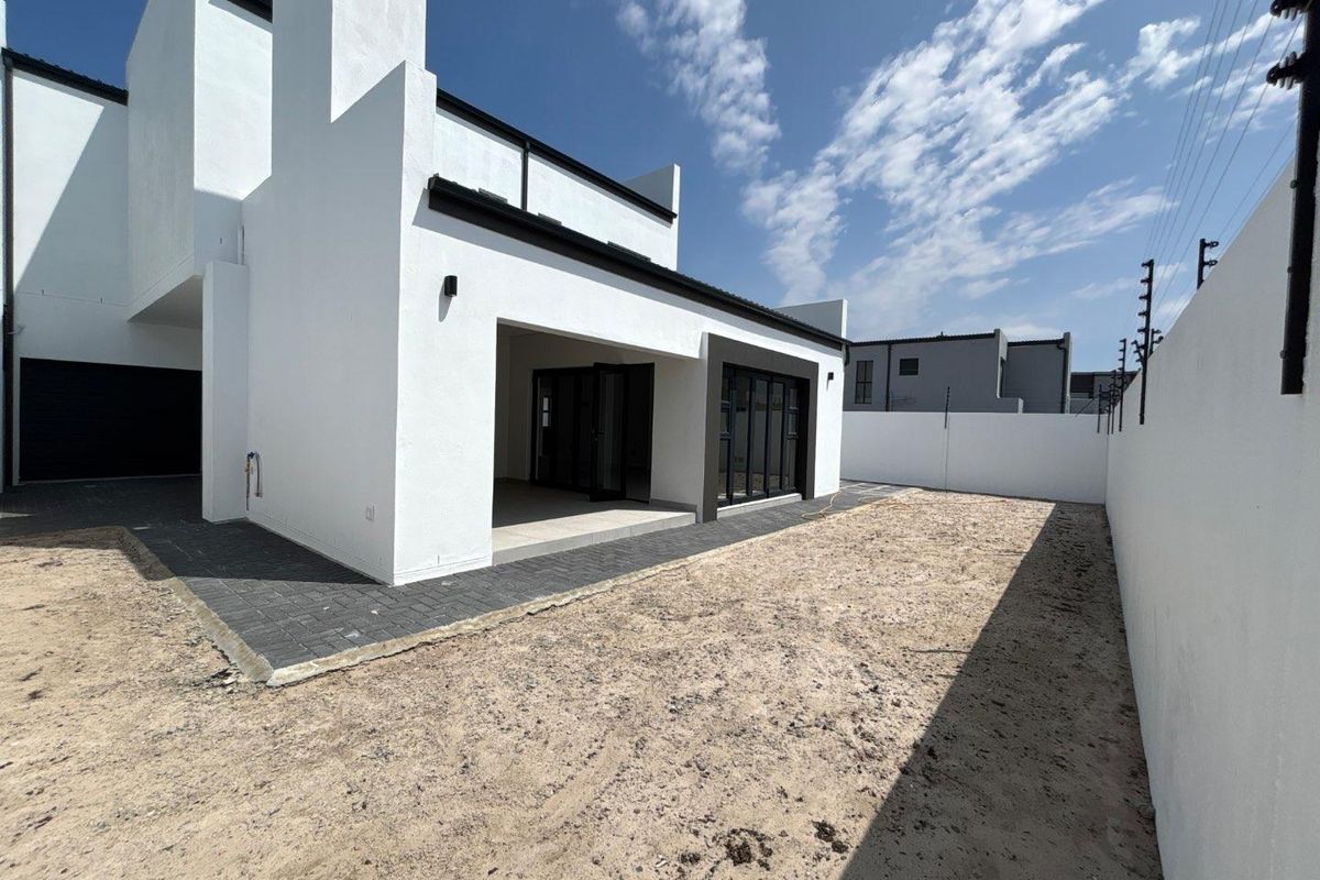 Rear view of a modern home featuring a covered patio, paved walkway, and an expansive, unlandscaped garden area enclosed by a perimeter wall.