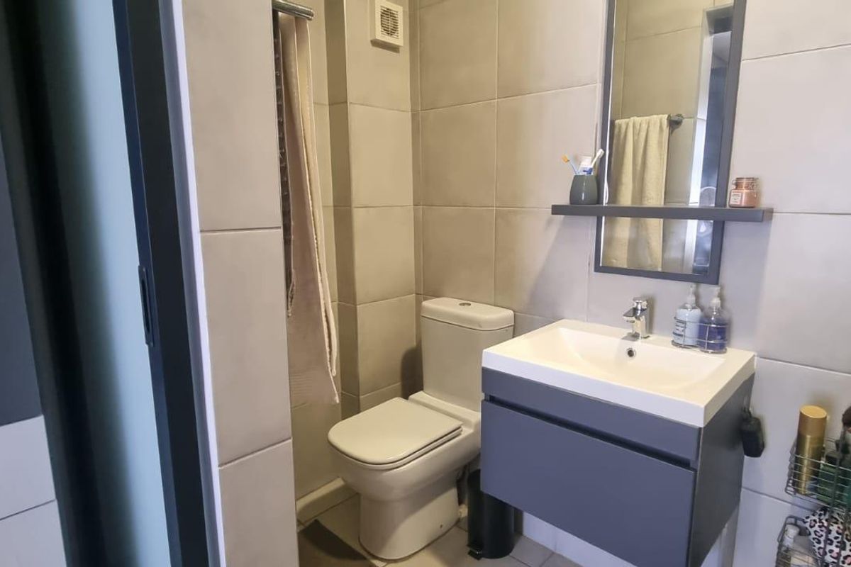 A modern, compact bathroom featuring a wall-mounted vanity with a basin, a toilet, and neutral wall tiling.