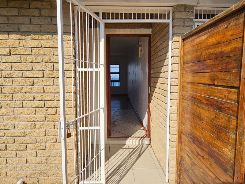 Exterior entrance area featuring a brick facade, secure metal gate, and tiled flooring leading into the interior hallway.