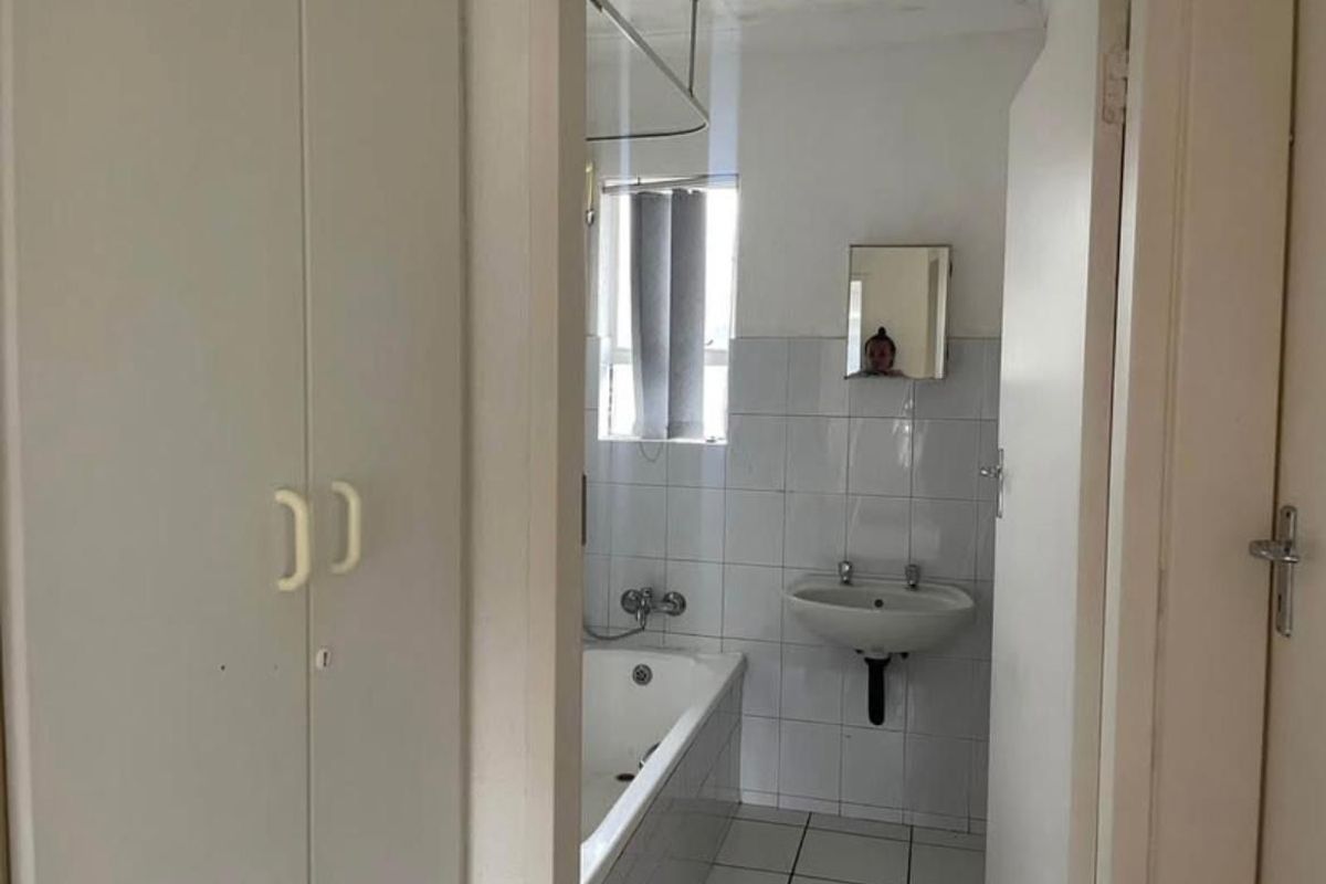 A functional bathroom featuring a bathtub, wall-mounted basin, and tiled finishes, requiring cosmetic updates to modernize the space.