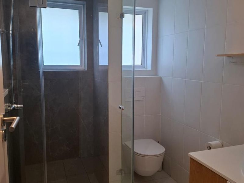 Modern bathroom featuring a glass-enclosed walk-in shower, wall-mounted toilet, and a sleek vanity cabinet with clean tiled finishes.