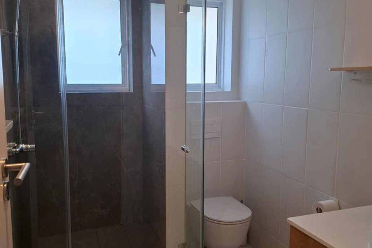 Modern bathroom featuring a glass-enclosed walk-in shower, wall-mounted toilet, and a sleek vanity cabinet with clean tiled finishes.