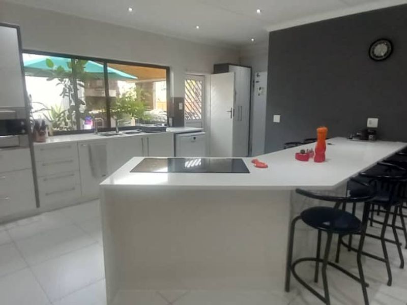Modern kitchen featuring a large island with breakfast bar, sleek white cabinetry, integrated oven, induction hob, and high-quality tiled flooring.