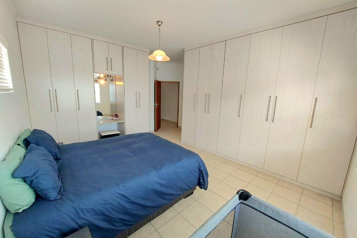 Spacious bedroom featuring extensive floor-to-ceiling built-in cabinetry with a central vanity area and neutral tiled flooring.