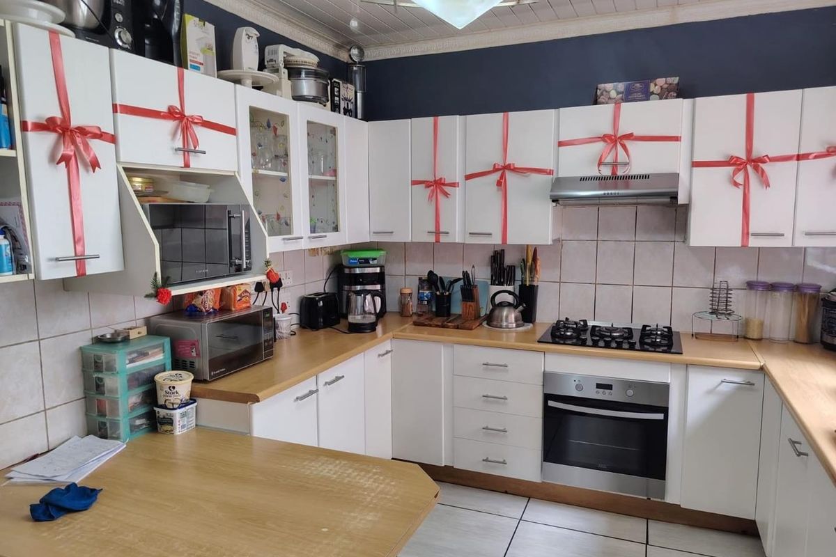 A functional kitchen featuring white cabinetry, a built-in gas hob, an under-counter oven, and a stainless steel extractor fan with tiled splashbacks.